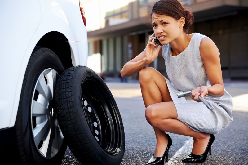 Woman calling for assistance with flat tire on car in the city